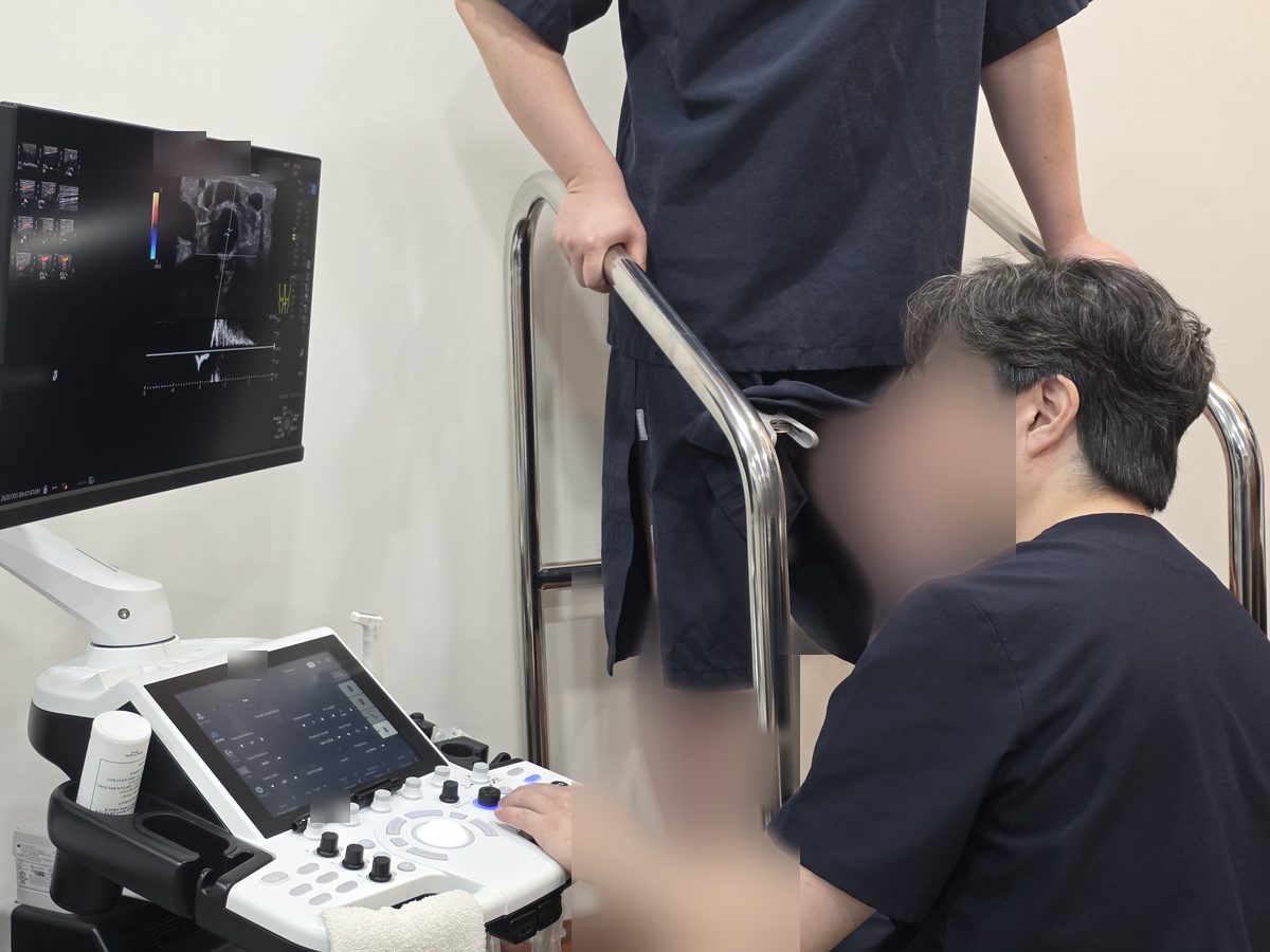의료진이 초음파 장비로 서 있는 환자의 다리를 검사하는 장면입니다.