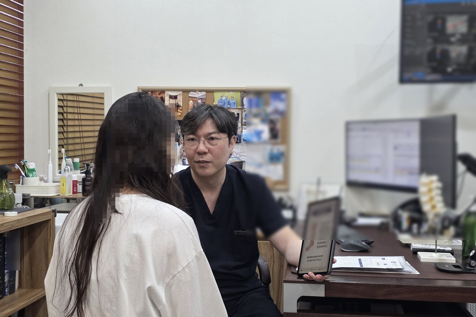 진료실에서 의사가 태블릿을 보여 주며 환자에게 상담하는 모습.