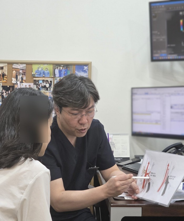 의사가 진료실에서 혈관 그림이 있는 자료를 보며 환자에게 치료를 설명하는 장면.