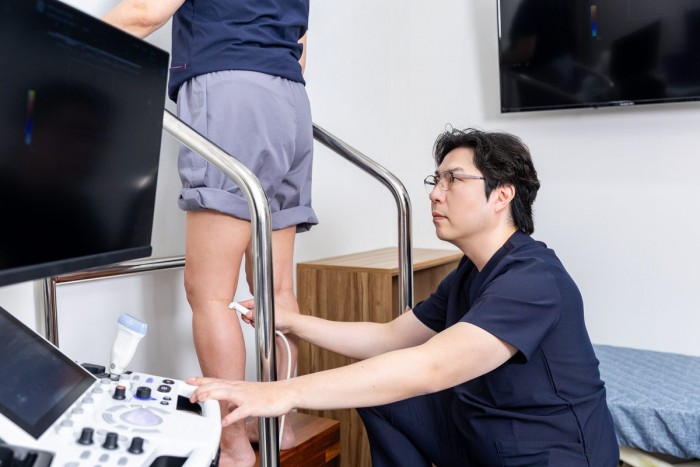 김서전 대표원장이 서 있는 환자의 다리를 도플러 초음파로 검사하는 모습